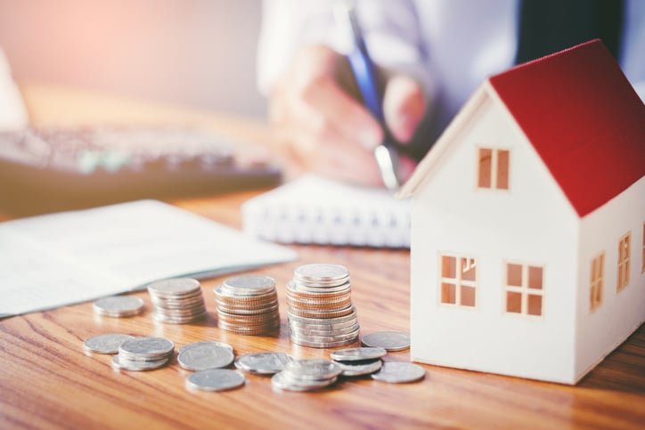 man doing calculations on a notepad, with coins and a house