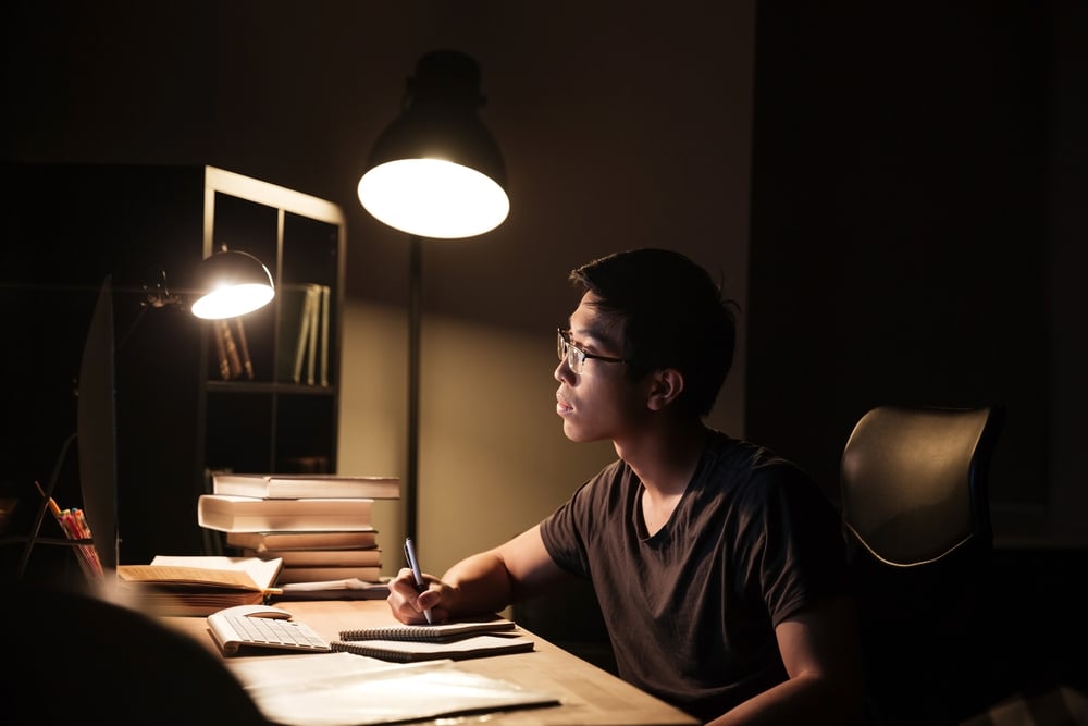 A boy studying with only his desk lamp lighted.
