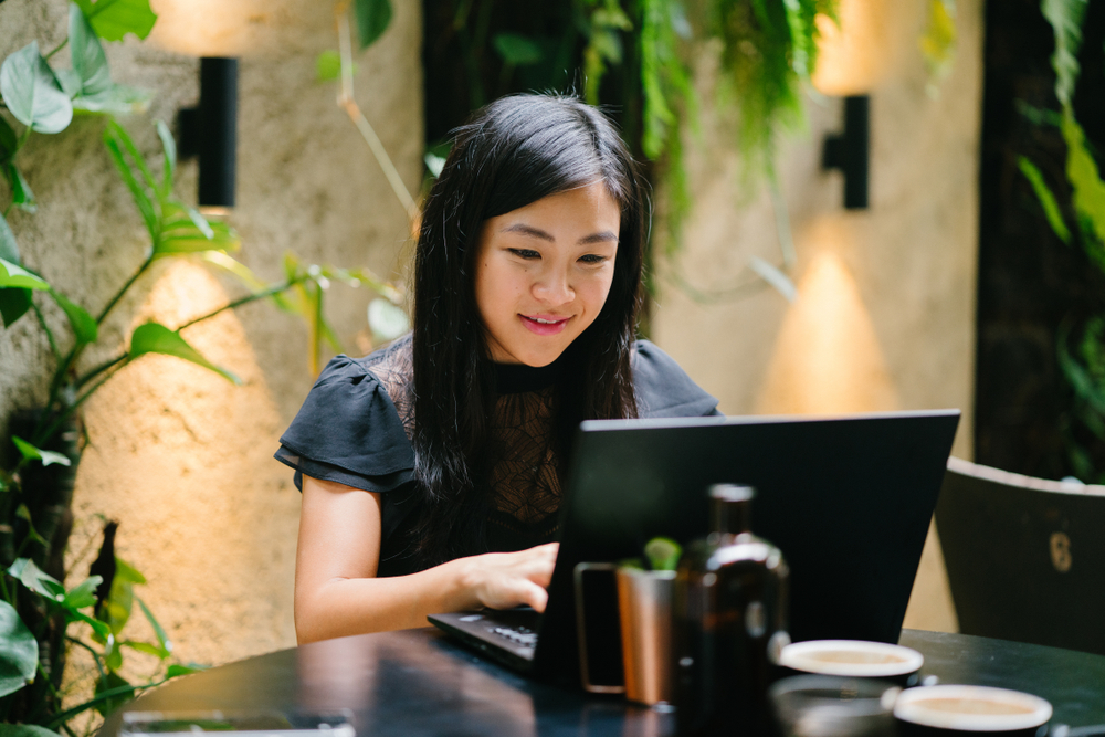 woman working in front of her laptop in an office with plants behind her
