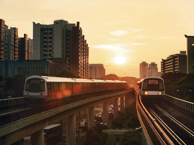 Two MRT trains on the tracks with a sunset behind