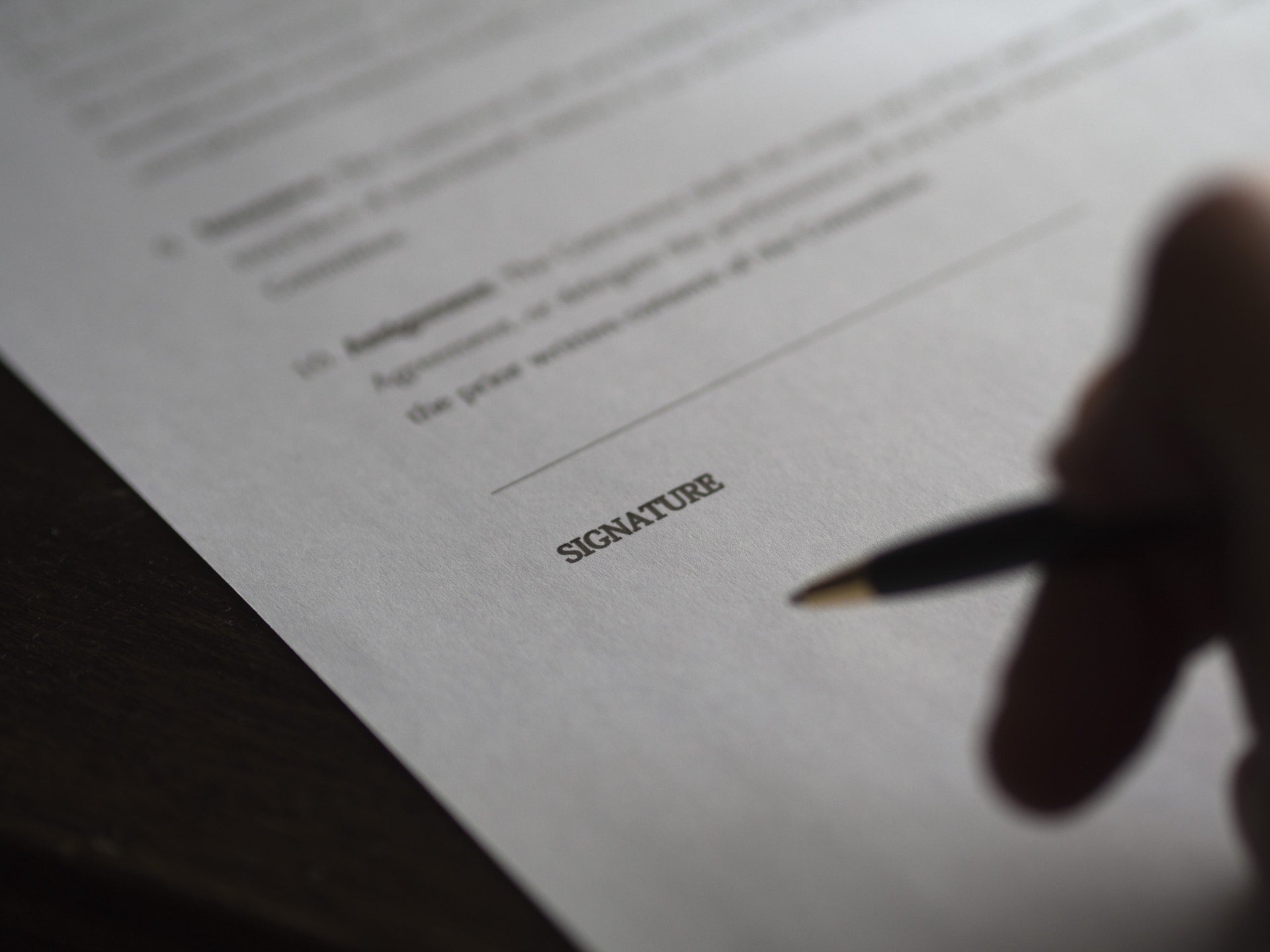 Someone pausing just before signing on the dotted line of a document.