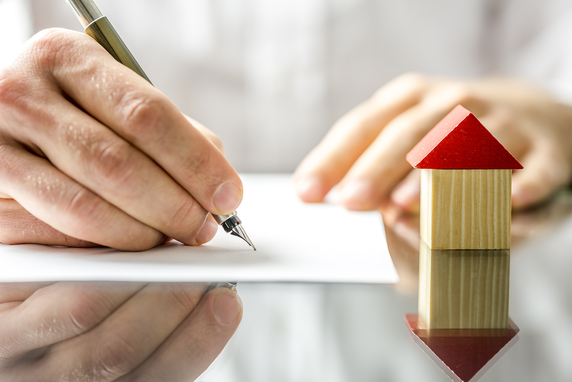 A man signing a document for his home loan, with a small wooden house beside his hand.