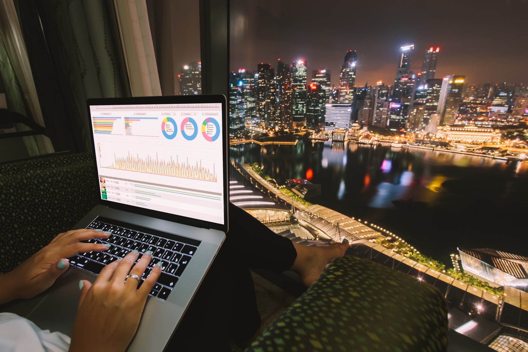 Looking out at Singapore city with an open laptop, showing graphs