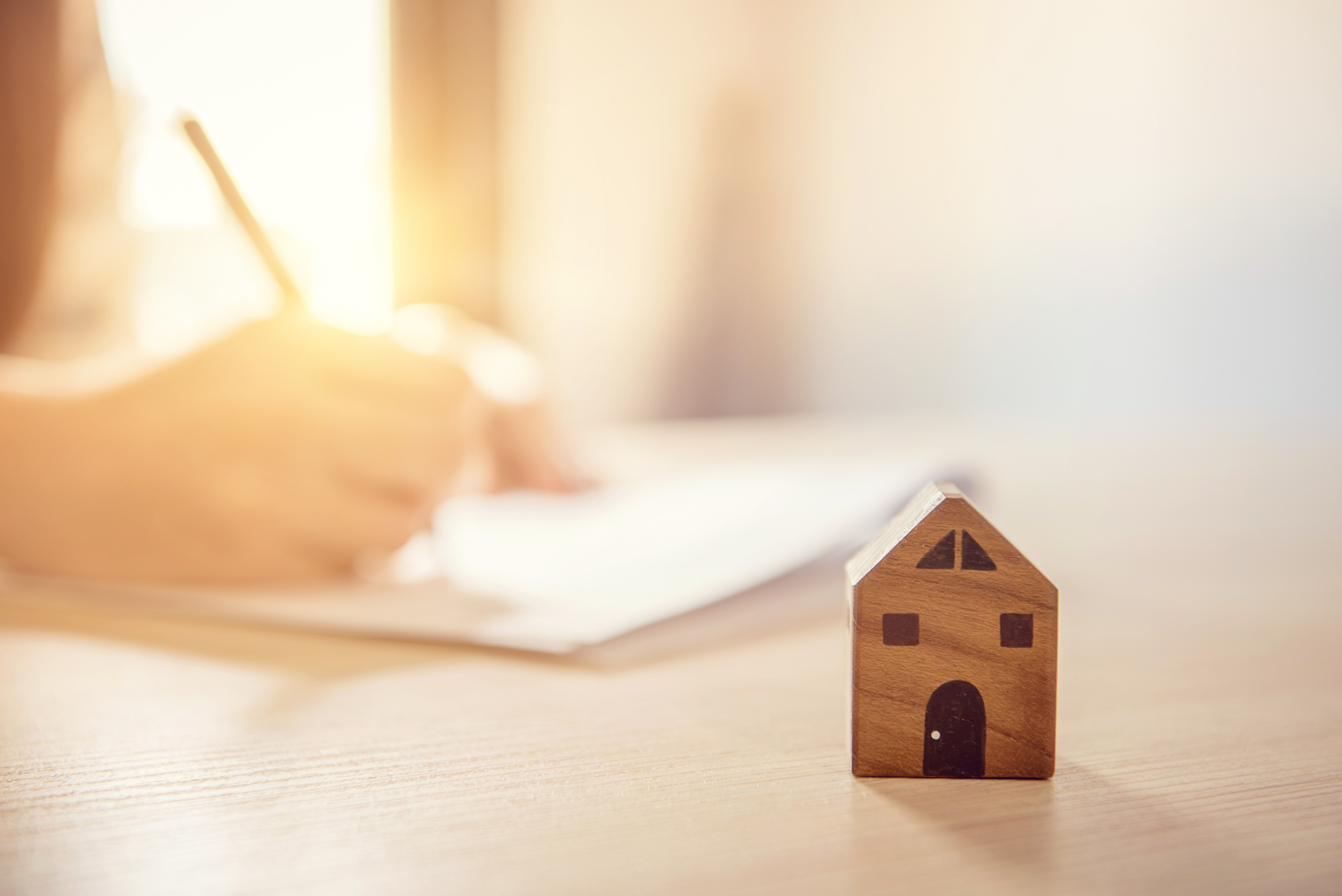 Wooden toy house with Woman signs a purchase contract or mortgage for home, Real estate concept.