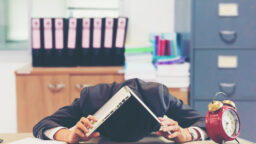 Man holding a laptop over his head bent over a table