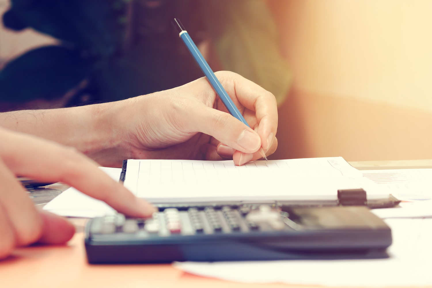 A person writing notes and using the calculator 
