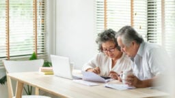 elderly man and woman looking at laptop and paper
