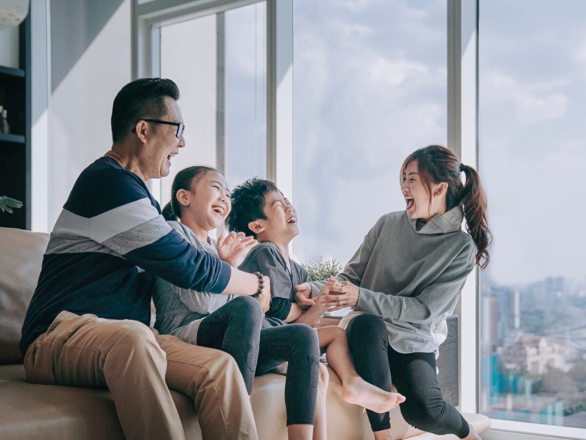 Asian chinese 2 parent tickling playing with their children at home in living room cuddle on sofa
