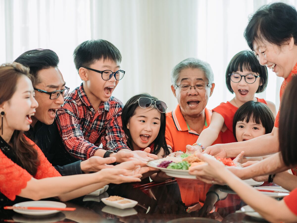Asian chinese family holding raw fish salad “Yusheng” with excited face during chinese new year's eve reunion dinner